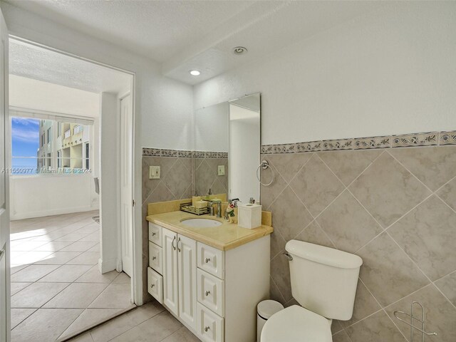 bathroom featuring vanity, tile flooring, toilet, and tile walls