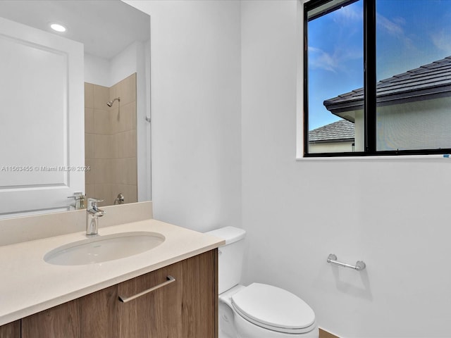 bathroom with tiled shower, vanity, and toilet