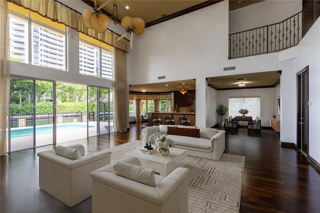 living room featuring dark hardwood / wood-style floors, a healthy amount of sunlight, a towering ceiling, and crown molding