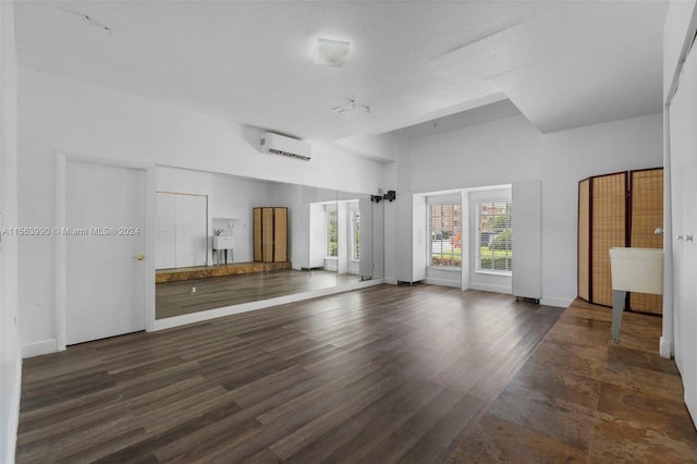 unfurnished living room with a textured ceiling, a wall unit AC, and dark wood-type flooring