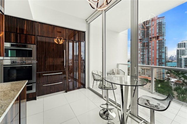 kitchen featuring modern cabinets, light stone countertops, stainless steel double oven, a city view, and floor to ceiling windows