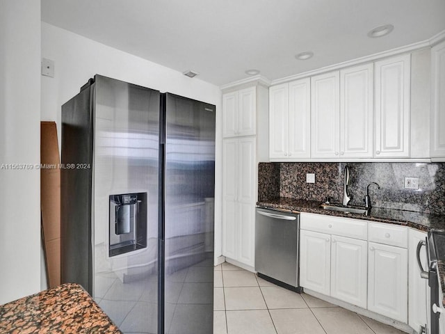 kitchen featuring white cabinetry, stainless steel appliances, light tile floors, tasteful backsplash, and dark stone countertops