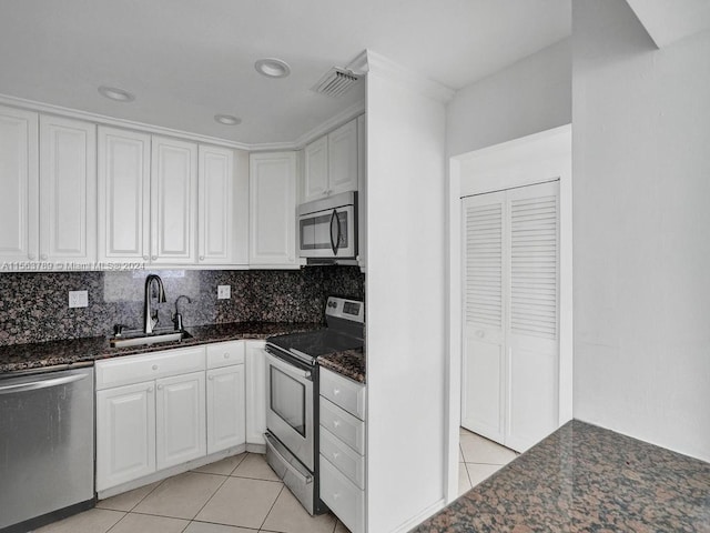 kitchen with appliances with stainless steel finishes, light tile floors, white cabinets, tasteful backsplash, and dark stone countertops