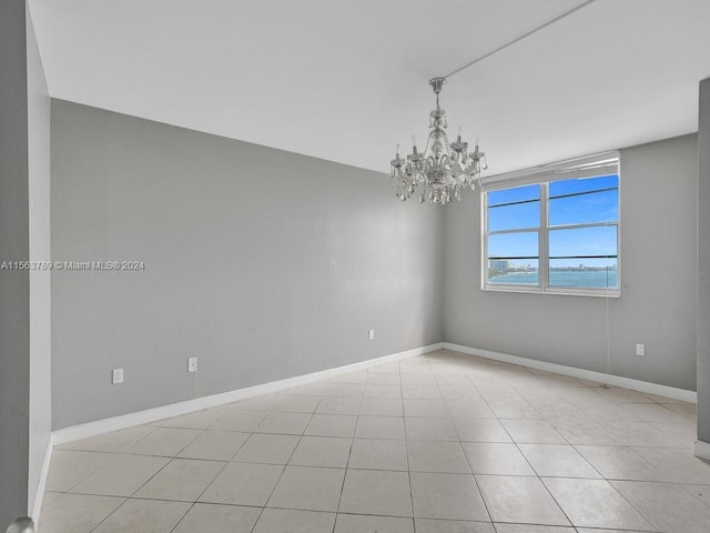 tiled spare room with a notable chandelier