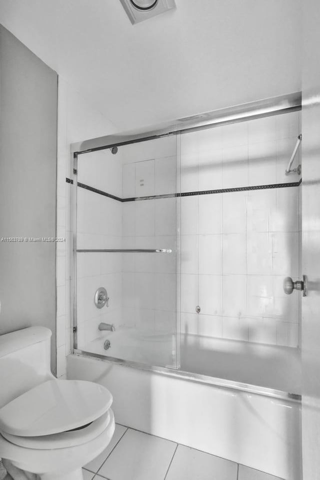 bathroom featuring toilet, combined bath / shower with glass door, and tile flooring