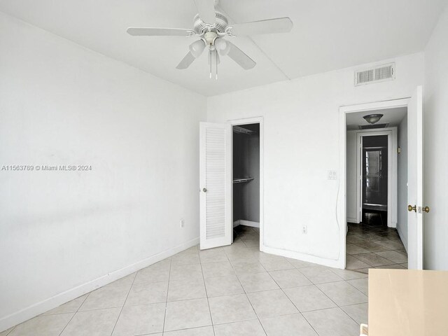 unfurnished bedroom featuring a spacious closet, a closet, ceiling fan, and light tile flooring