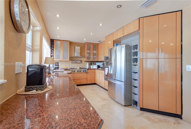 kitchen featuring dark stone countertops, appliances with stainless steel finishes, wall chimney exhaust hood, sink, and light tile floors