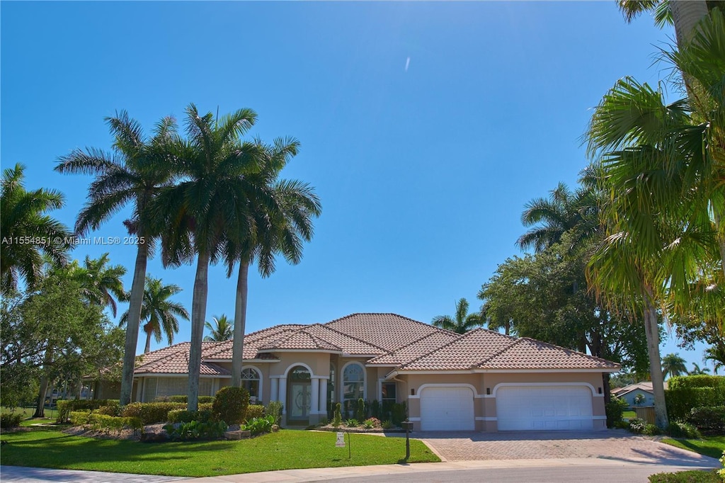 mediterranean / spanish-style house featuring a garage, decorative driveway, a front yard, and stucco siding