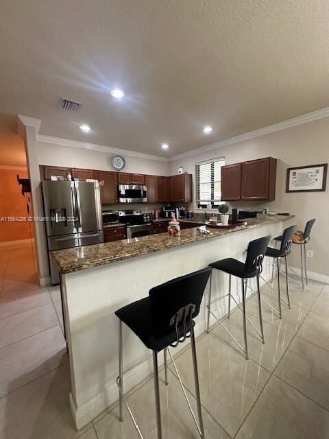 kitchen featuring a breakfast bar area, ornamental molding, appliances with stainless steel finishes, and light tile flooring