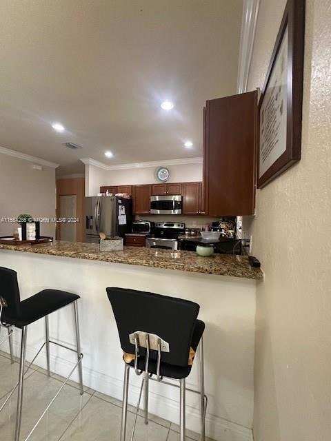 kitchen with a kitchen breakfast bar, light tile floors, kitchen peninsula, appliances with stainless steel finishes, and dark stone countertops