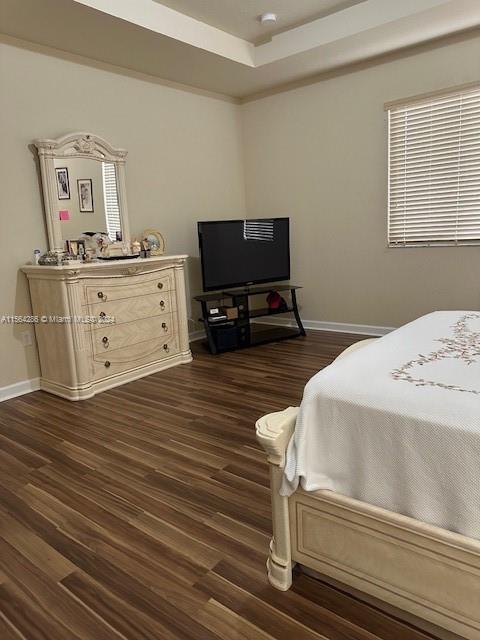 bedroom with a raised ceiling and dark hardwood / wood-style floors