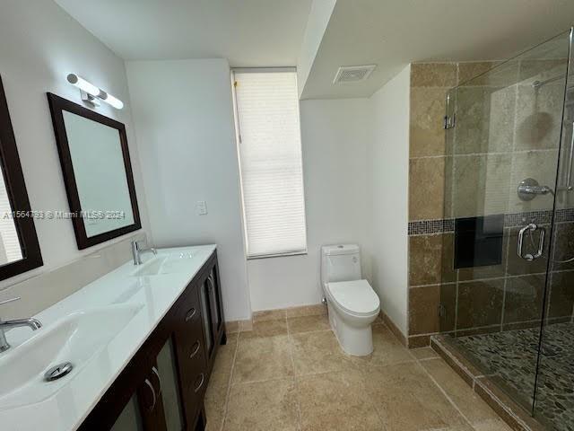 bathroom with toilet, tile floors, dual bowl vanity, and a shower with door