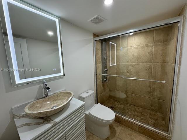 bathroom with tile flooring, toilet, vanity, and a shower with shower door