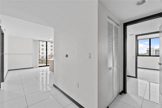 hallway with a wealth of natural light, a wall of windows, and light tile patterned flooring