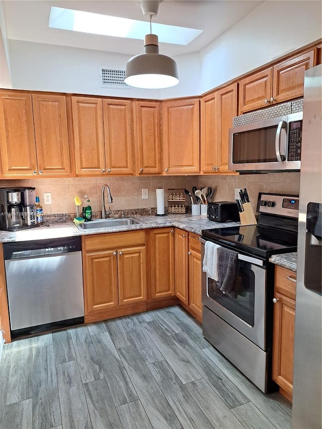 kitchen with a skylight, hanging light fixtures, sink, stainless steel appliances, and tasteful backsplash