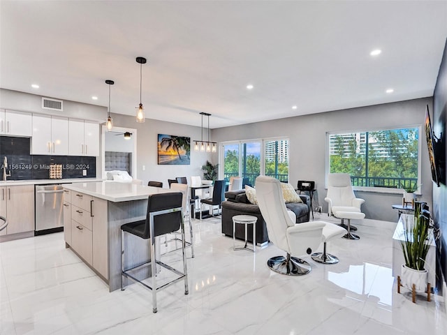 kitchen featuring stainless steel dishwasher, a center island, a breakfast bar area, decorative light fixtures, and white cabinets