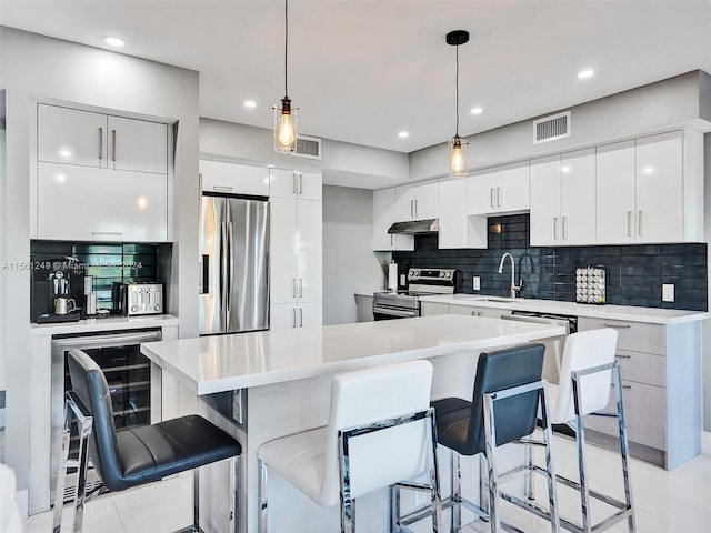 kitchen featuring white cabinets, stainless steel appliances, backsplash, hanging light fixtures, and light tile flooring