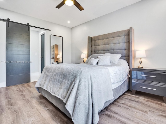 bedroom with a barn door, light hardwood / wood-style floors, and ceiling fan