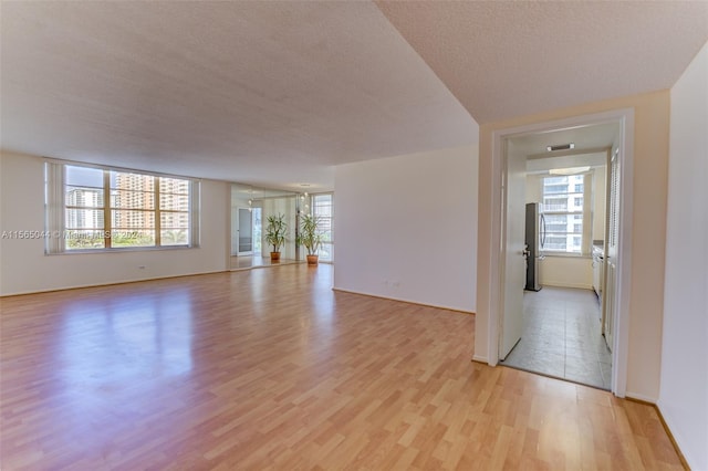 empty room with a textured ceiling, a healthy amount of sunlight, and light wood-type flooring