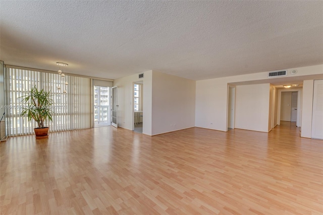 empty room featuring a textured ceiling, light wood-type flooring, and a wall of windows