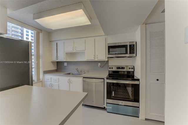 kitchen with stainless steel appliances, backsplash, light tile floors, sink, and white cabinetry