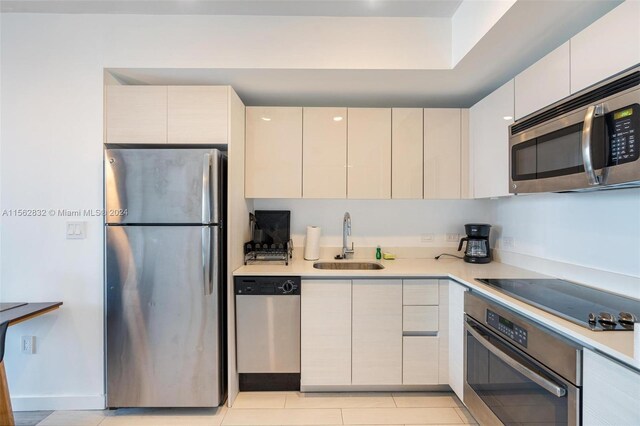 kitchen featuring appliances with stainless steel finishes, cream cabinetry, sink, and light tile floors