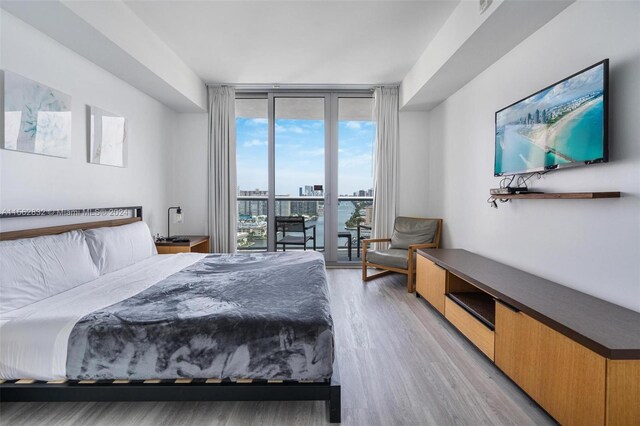 bedroom with light hardwood / wood-style floors, access to outside, and a wall of windows