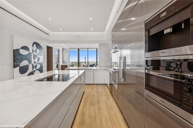 kitchen featuring black electric cooktop, white cabinetry, light hardwood / wood-style flooring, stainless steel double oven, and light stone counters