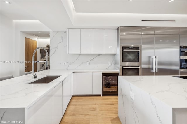 kitchen with light stone countertops, light wood-type flooring, backsplash, appliances with stainless steel finishes, and sink