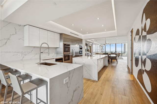 kitchen with light stone counters, white cabinets, sink, a raised ceiling, and light hardwood / wood-style flooring