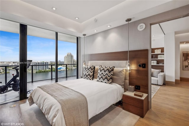 bedroom with expansive windows, a water view, light wood-type flooring, and access to outside