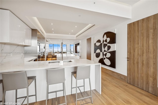 kitchen with white cabinets, a raised ceiling, sink, and a breakfast bar