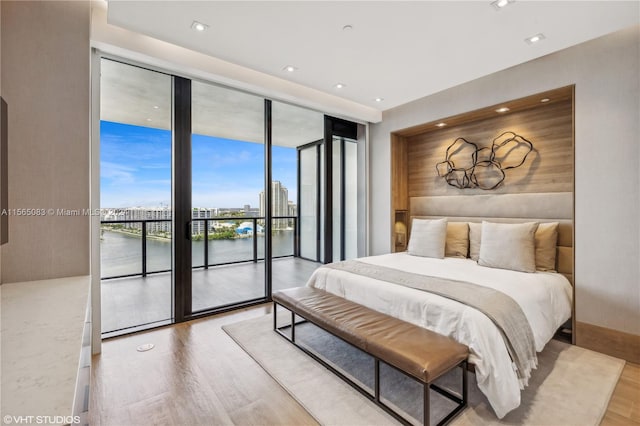 bedroom featuring floor to ceiling windows, a water view, light wood-type flooring, and access to outside