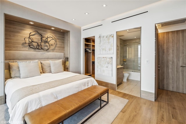 bedroom with a closet, connected bathroom, a spacious closet, and light wood-type flooring