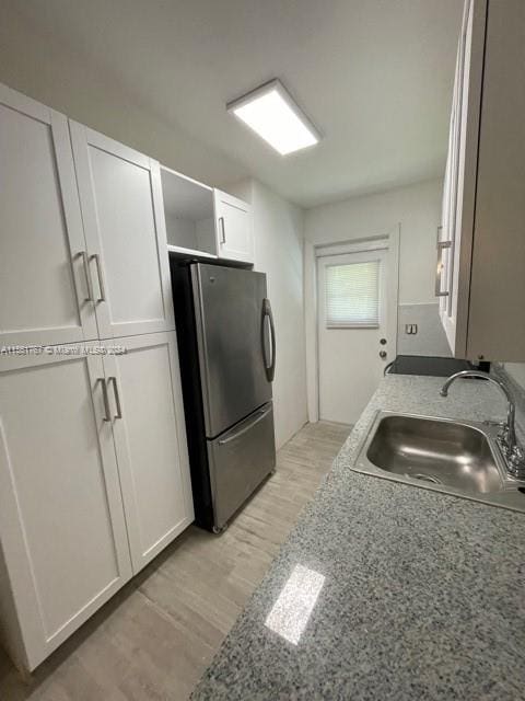 kitchen with light stone countertops, stainless steel fridge, sink, light wood-type flooring, and white cabinets