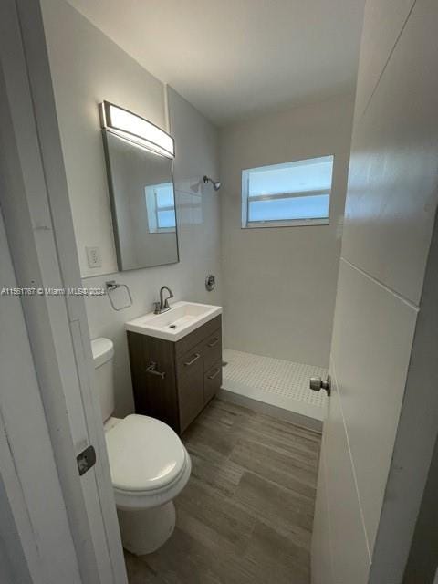 bathroom featuring hardwood / wood-style flooring, toilet, vanity, and tiled shower