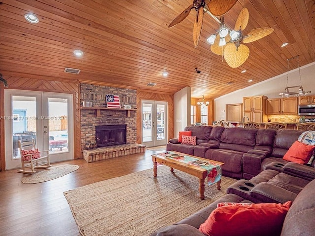 living room with a brick fireplace, vaulted ceiling, ceiling fan, french doors, and light wood-type flooring