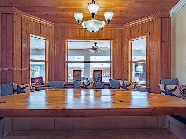 dining area featuring crown molding, ceiling fan with notable chandelier, wooden walls, and plenty of natural light