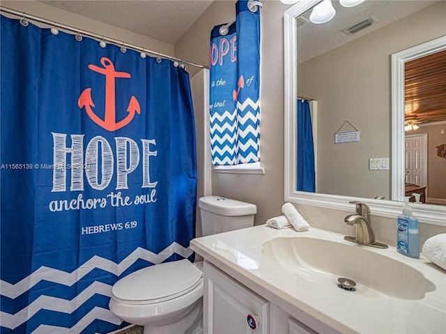 bathroom with ceiling fan, a textured ceiling, vanity with extensive cabinet space, and toilet