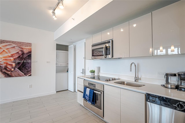 kitchen featuring stainless steel appliances, rail lighting, stacked washer / dryer, white cabinets, and sink