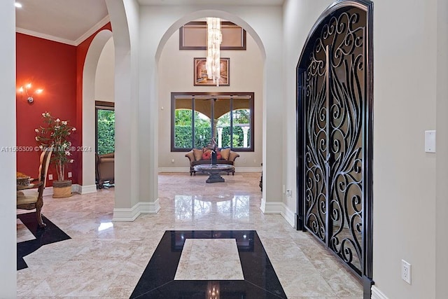 foyer entrance with light tile flooring, crown molding, a towering ceiling, and an inviting chandelier