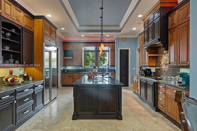 kitchen featuring hanging light fixtures, dark stone counters, a raised ceiling, built in refrigerator, and ornamental molding