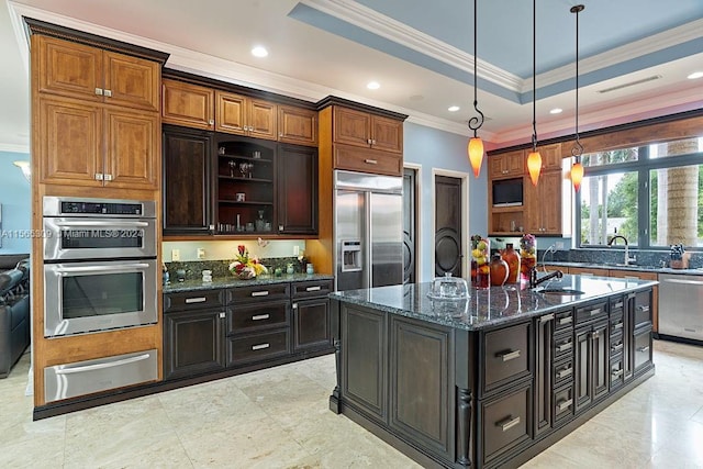 kitchen featuring hanging light fixtures, ornamental molding, appliances with stainless steel finishes, a tray ceiling, and a kitchen island with sink