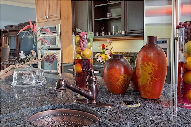 kitchen featuring dark stone counters, stainless steel double oven, and ornamental molding