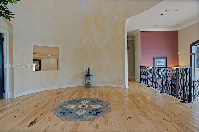 empty room featuring ornamental molding, light wood-type flooring, and a high ceiling