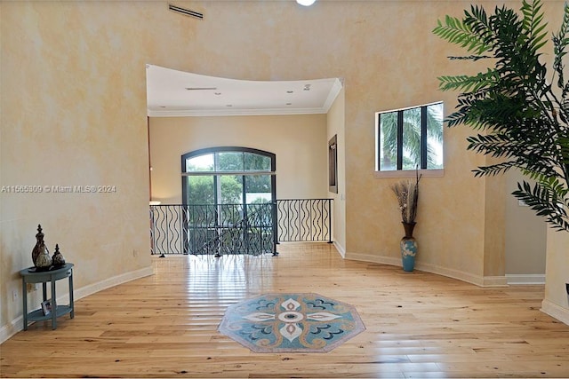 unfurnished room with light hardwood / wood-style flooring, ornamental molding, and a towering ceiling