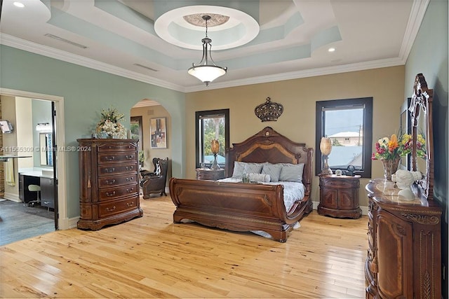 bedroom featuring ornamental molding, ensuite bathroom, a tray ceiling, and light wood-type flooring