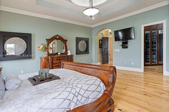 bedroom featuring ornamental molding, a tray ceiling, and light hardwood / wood-style flooring