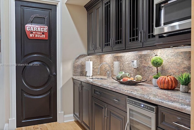 kitchen with light stone counters, tasteful backsplash, wine cooler, light hardwood / wood-style flooring, and sink