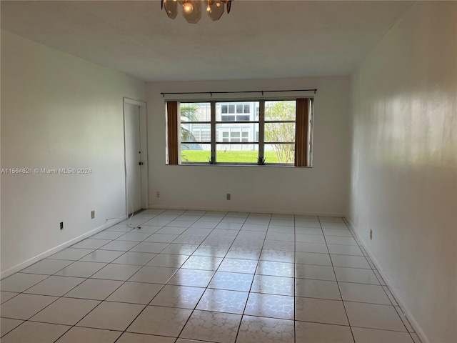 tiled empty room featuring an inviting chandelier